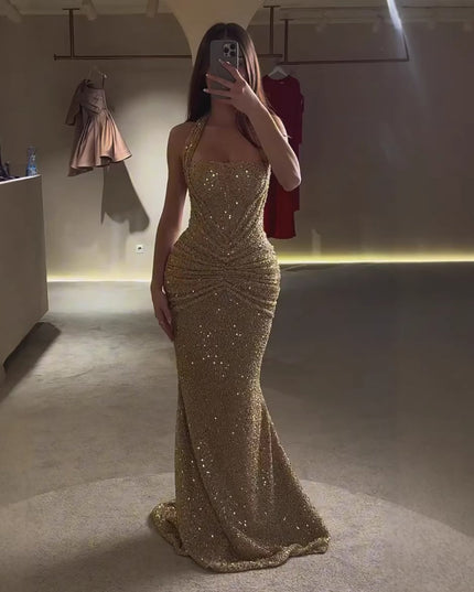 Gold sequin halter maxi dress shown in mirror with fitted shape and floor-length hem, side view