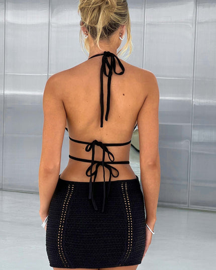 Back view of a black crochet mini dress showing halter neck ties and exposed back, with intricate knit details.