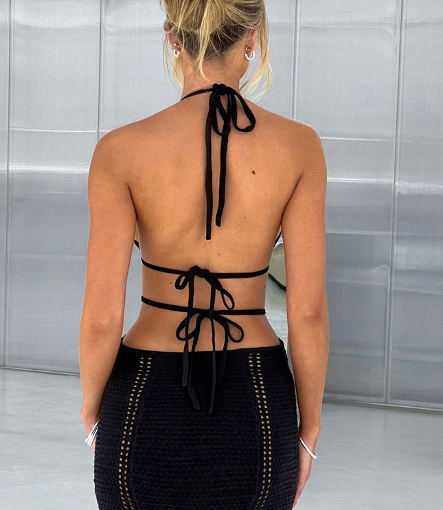 Back view of a black crochet mini dress showing halter neck ties and exposed back, with intricate knit details.