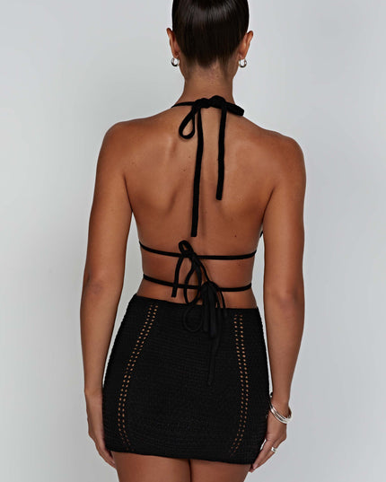 Rear view of the black crochet mini dress, showing the halter neck tie-up and back details on a woman with dark hair.