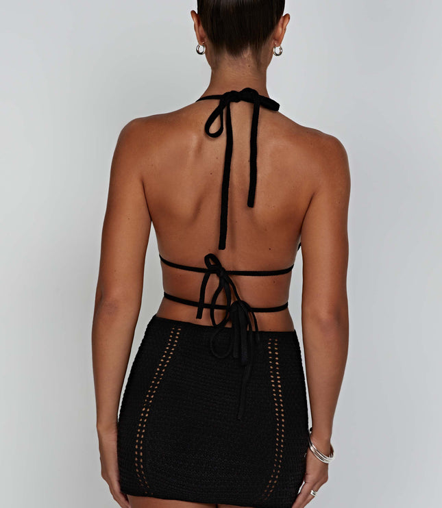 Rear view of the black crochet mini dress, showing the halter neck tie-up and back details on a woman with dark hair.
