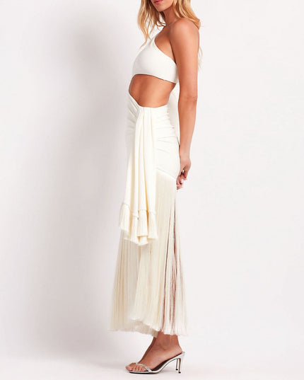 Side profile of the white one-shoulder cut-out maxi dress, showing the full fringe skirt and draped detail.