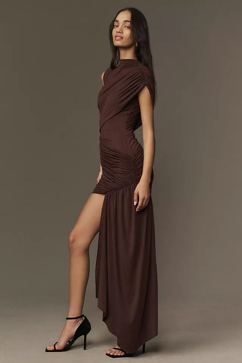 Side profile of a brown ruched asymmetrical mini maxi dress, showcasing the high leg slit and flowing skirt detail.