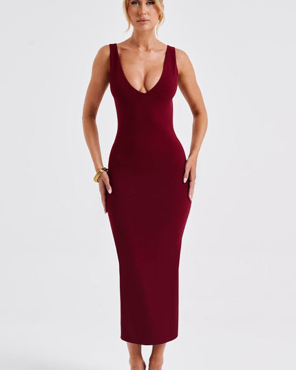 Form-fitting women's burgundy plunge neck midi dress with a low back design, styled with clear heels.