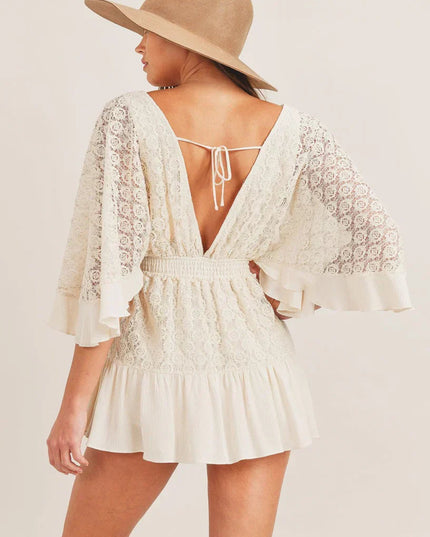 Back view of the cream lace V-neck mini romper, a deep V-back with tie detail and flowy sleeves.
