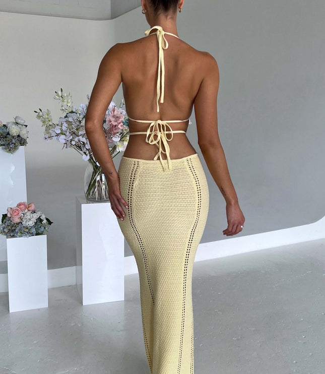 Back view of a women's light yellow crochet knit maxi dress, showing the halter tie closure and open back design.