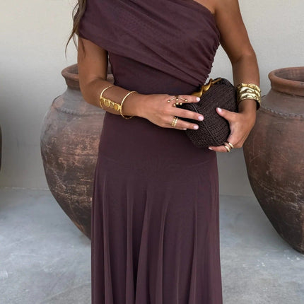 Women's chocolate brown drape one shoulder mesh maxi dress, styled with gold jewelry and a woven clutch.