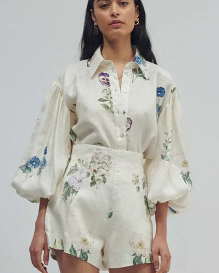 Women's white linen short set with colorful floral print, featuring a button-down balloon sleeve top and high-waisted shorts.