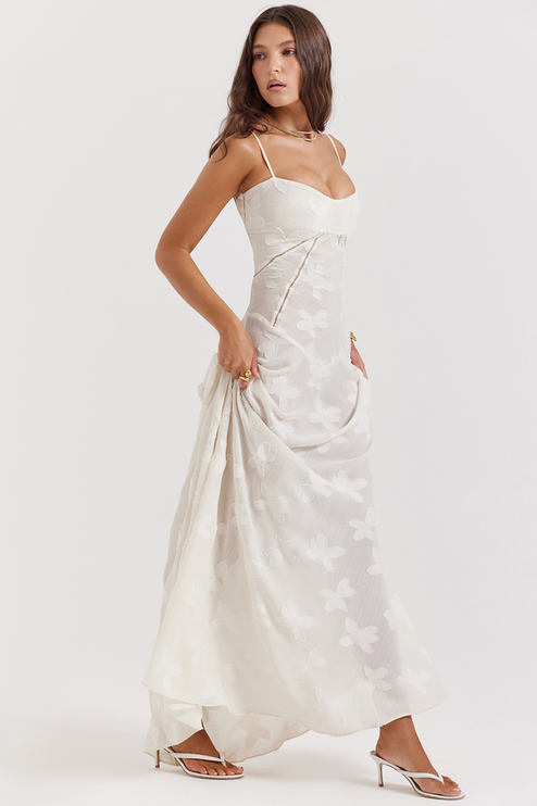 White floral corset maxi dress with a full skirt and butterfly- floral texture, worn with white heeled sandals, showcasing the dress's movement.