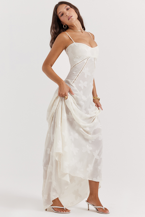 Side view of a white floral corset maxi dress with a full skirt, showing the intricate butterfly- pattern and the dress's flow.