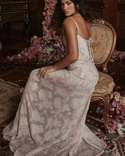 Side view of a light pink floral corset maxi dress with a lace-up back, sitting on an ornate chair.
