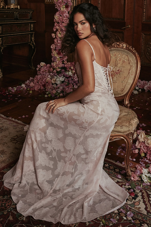 Side view of a light pink floral corset maxi dress with a lace-up back, sitting on an ornate chair.