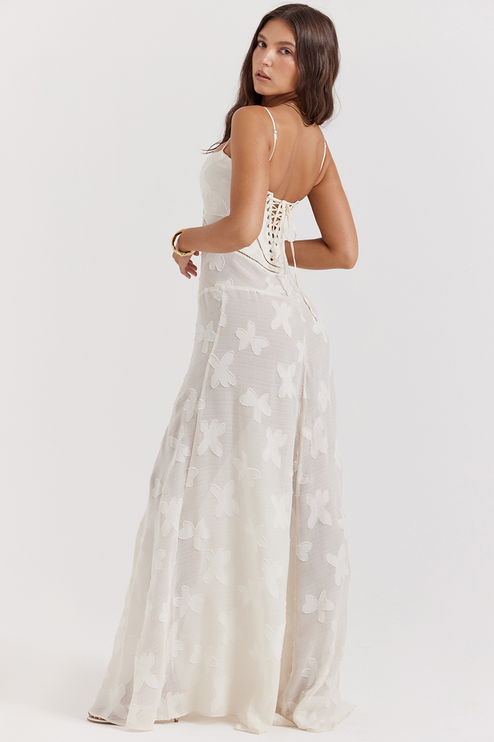 Side view of a white floral corset maxi dress with a lace-up back and delicate butterfly- floral pattern on the full skirt.