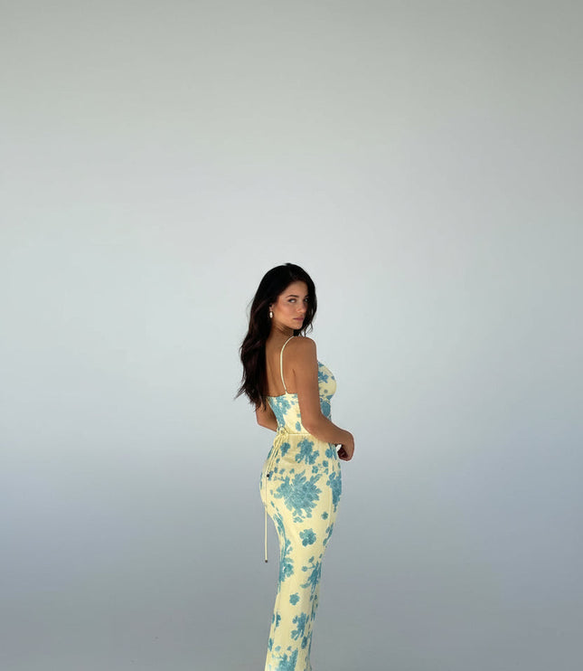 Back view of a women's yellow floral maxi dress showing the adjustable straps and subtle side ruching, with blue floral pattern.