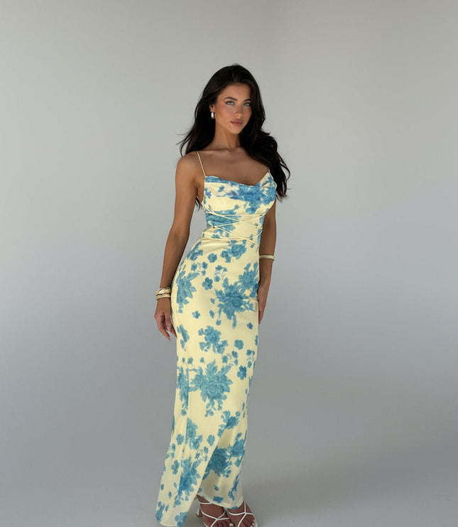 Full-length view of a women's yellow floral cowl neck maxi dress with blue flowers and adjustable straps, paired with white heels.