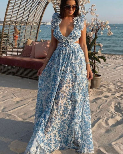 Women's blue and white floral print maxi dress on a beach, showcasing the flowing skirt and V-neck with ring detail.