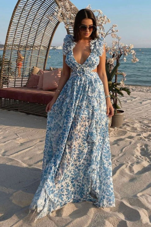 Women's blue and white floral print maxi dress on a beach, showcasing the flowing skirt and V-neck with ring detail.