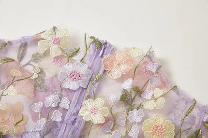 Close-up of the delicate floral embroidery on the sheer lavender fabric of the women's maxi prom dress.