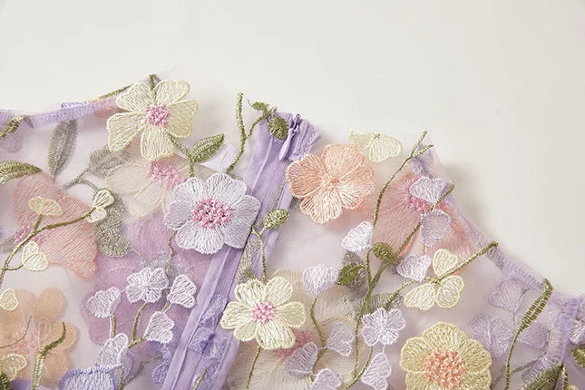 Close-up of the delicate floral embroidery on the sheer lavender fabric of the women's maxi prom dress.