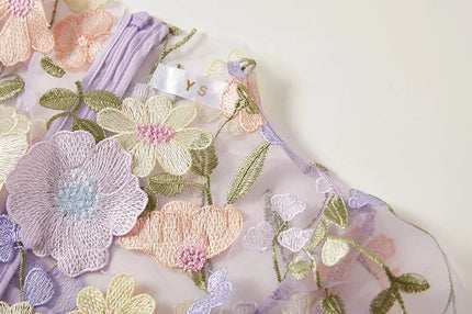 Detailed view of the colorful floral embroidery and sheer material of the women's lavender maxi prom dress, showing zipper detail.