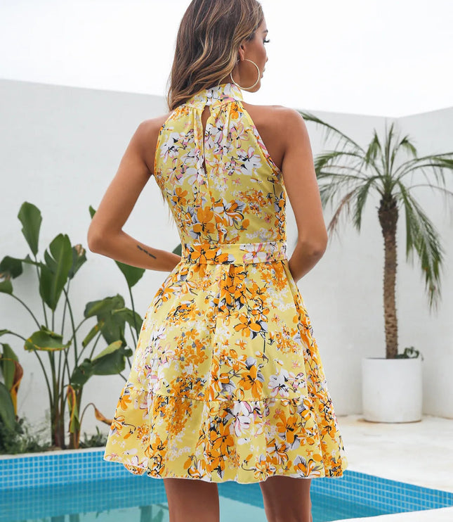 Back view of a yellow floral halter neck tiered mini dress, showing the keyhole and tied waist detail, with a palm tree in background.