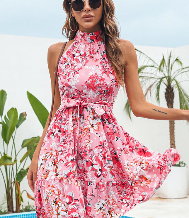 Pink floral halter neck tiered mini dress with a tie-waist, worn outdoors by a pool.