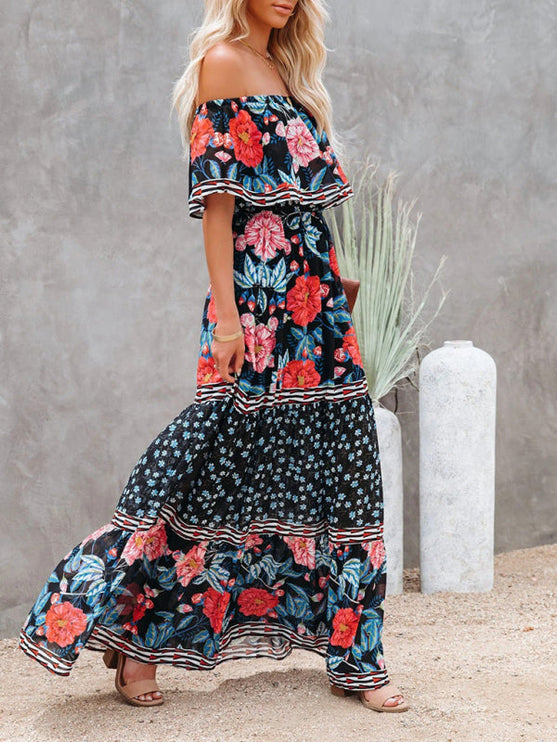 Side profile of a women's black floral off-shoulder maxi dress, showcasing red and blue flowers and a flowing skirt.