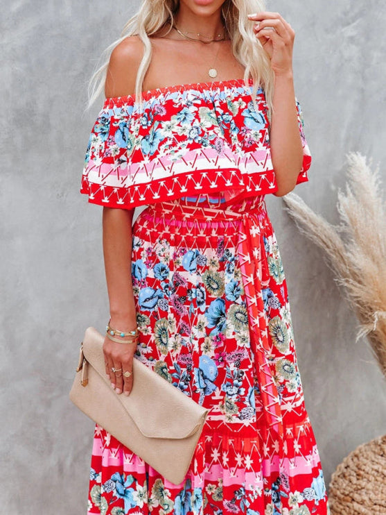 Close-up of red floral off-shoulder ruffled maxi dress with blue and white patterns, holding a beige clutch.