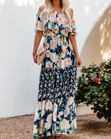 Women's off-shoulder ruffled floral maxi dress in navy blue with large peach and cream flowers, cinched waist, and tiered skirt.