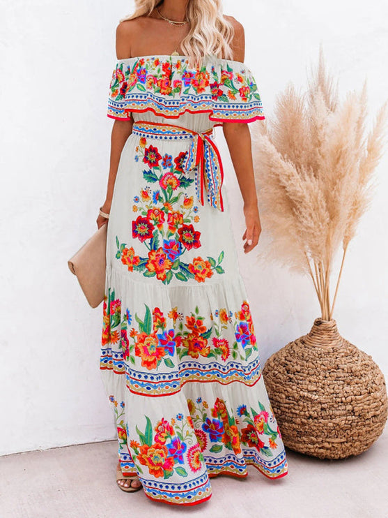 Women's off-shoulder white floral maxi dress with a red and blue patterned border, styled with a clutch.