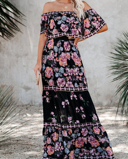 Women's off-shoulder ruffled maxi dress in black with pink and purple floral print, standing outdoors.