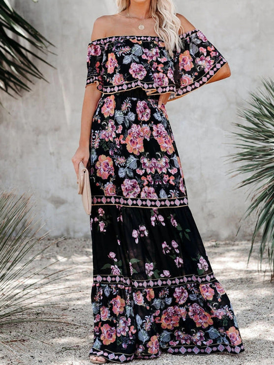 Women's off-shoulder ruffled maxi dress in black with pink and purple floral print, standing outdoors.