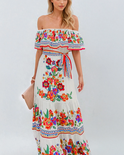 Women's off-shoulder ruffled maxi dress in white with vibrant red, orange, and blue floral print, tied at the waist.