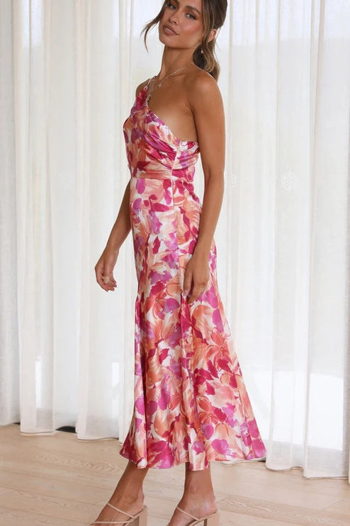 Side profile of a woman wearing a pink and orange floral one-shoulder ruched bust midi dress, with a flowing skirt.