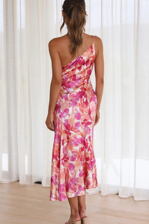 Back view of a woman in a vibrant pink and orange floral one-shoulder midi dress, showcasing the draped back.