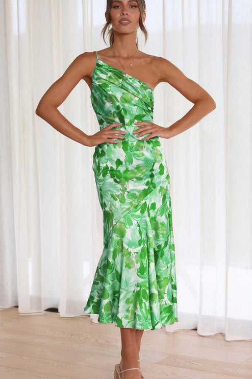 Front view of a woman wearing a green and white floral one-shoulder ruched bust midi dress, with hands on hips.