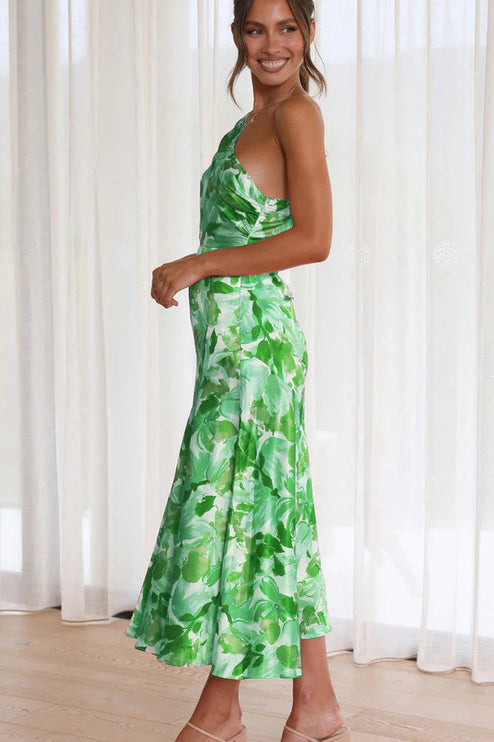 Side profile of a woman in a green and white floral one-shoulder midi dress, highlighting the elegant silhouette.