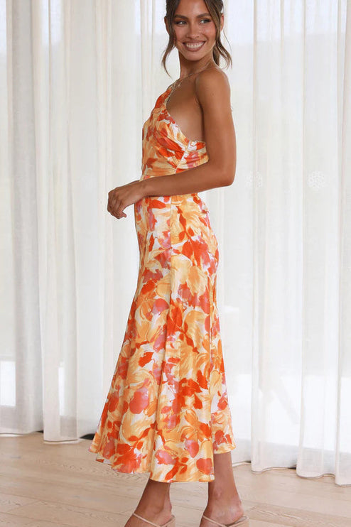 Side profile of a woman in an orange and white floral one-shoulder midi dress, showcasing the flowy fabric.