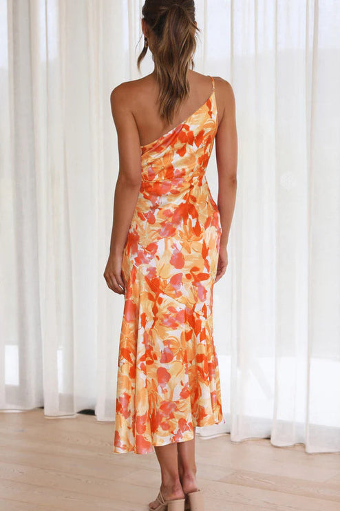Back view of a woman in an orange and white floral one-shoulder ruched bust midi dress, with a graceful drape.