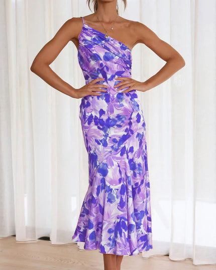 Front view of a woman wearing a purple and white floral one-shoulder ruched bust midi dress, with a stylish design.