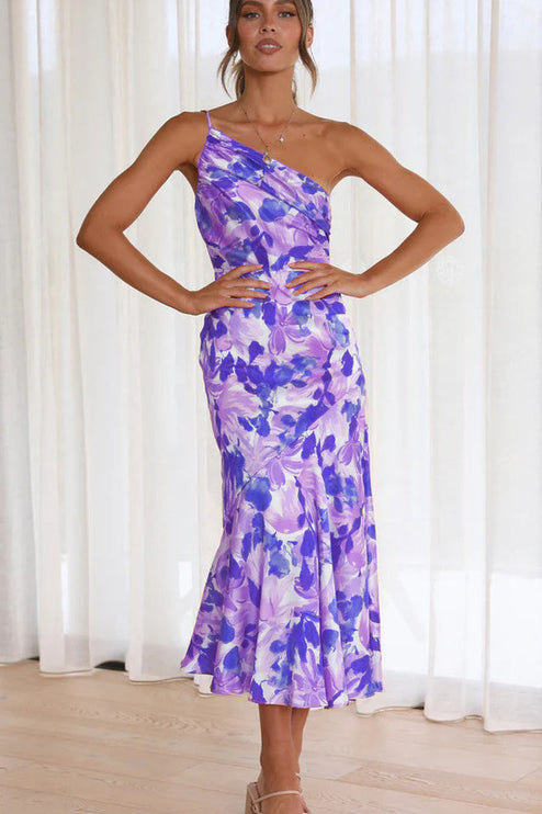 Front view of a woman wearing a purple and white floral one-shoulder ruched bust midi dress, with a stylish design.