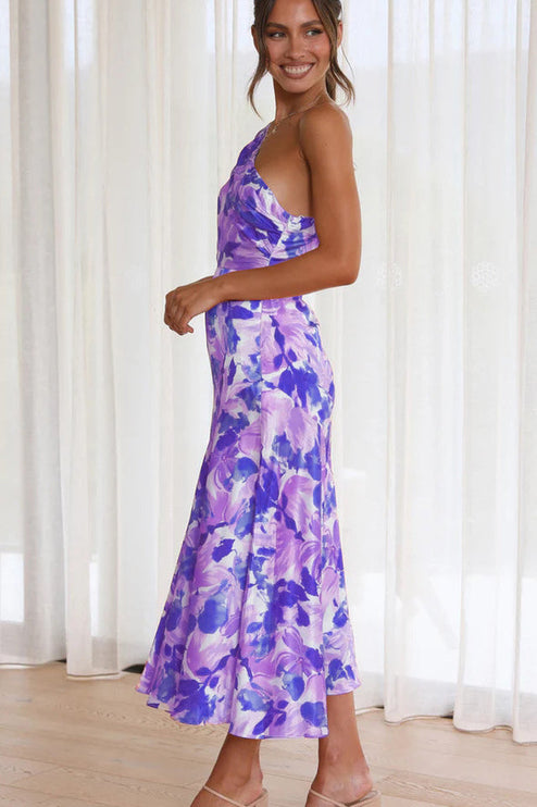 Side profile of a woman in a purple and white floral one-shoulder midi dress, highlighting the dress's cut and print.