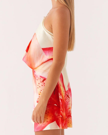 Side profile of a women's floral print cowl neck mini dress, highlighting the draped neckline and red and pink lily pattern.