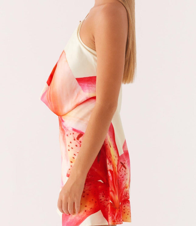 Side profile of a women's floral print cowl neck mini dress, highlighting the draped neckline and red and pink lily pattern.