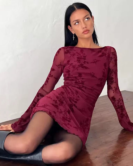 Maroon floral print long sleeve mini dress with boat neck, sheer sleeves, and lettuce hem, a woman sitting on a wooden floor.