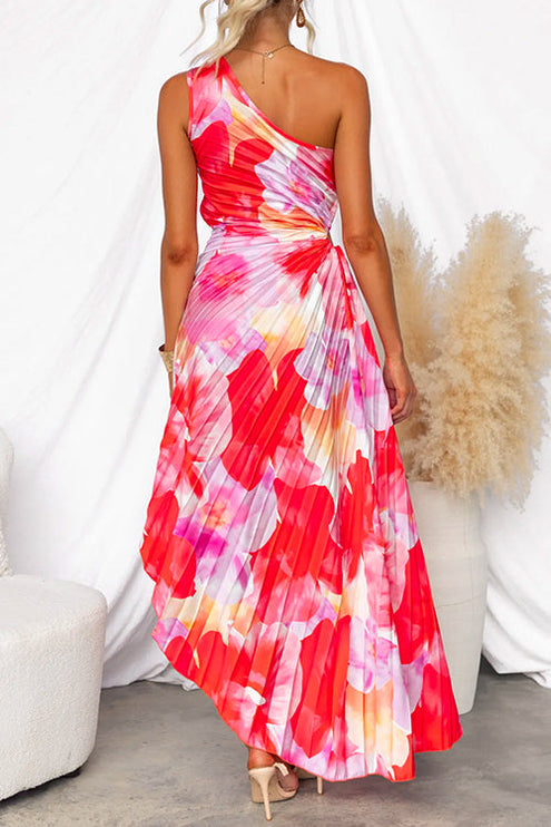 Back view of a vibrant red and pink floral print one-shoulder maxi dress with pleated skirt and cut-out detail at waist.