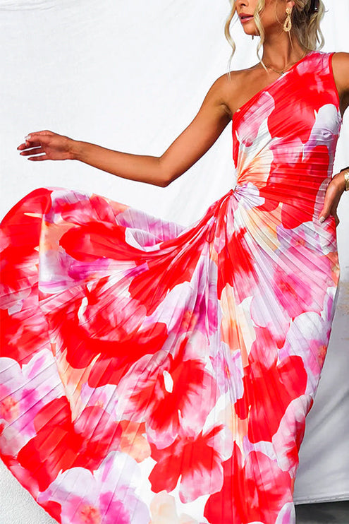 Close up of the flowing pleated skirt of a red and pink floral print one-shoulder maxi dress with cut-out.