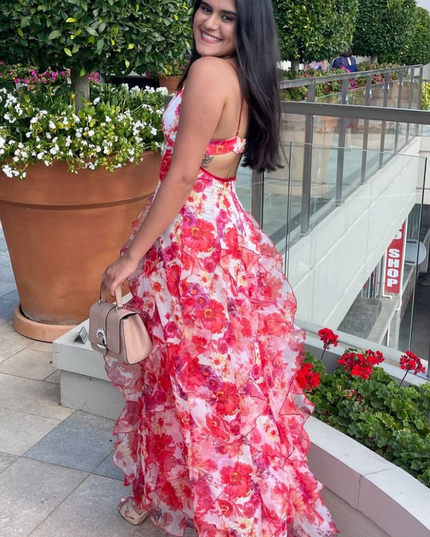 Side view of a woman in a floral print ruffled maxi dress with an open back and spaghetti straps, holding a purse.