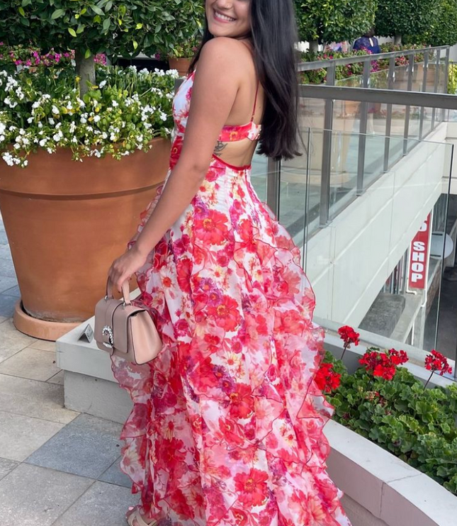 Side view of a woman in a floral print ruffled maxi dress with an open back and spaghetti straps, holding a purse.