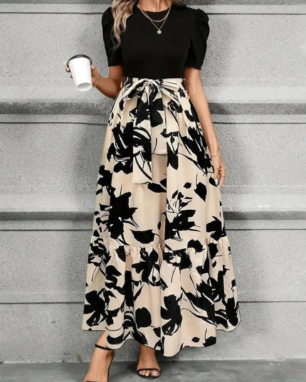Front view of a women's high waist maxi dress with a black floral print on beige, featuring a black short sleeve top and waist tie.